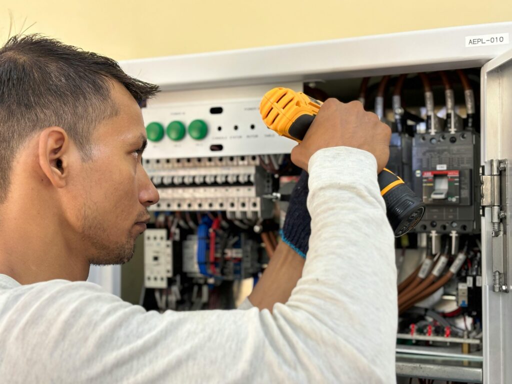 About Professional electrician using a drill on an indoor circuit breaker panel.